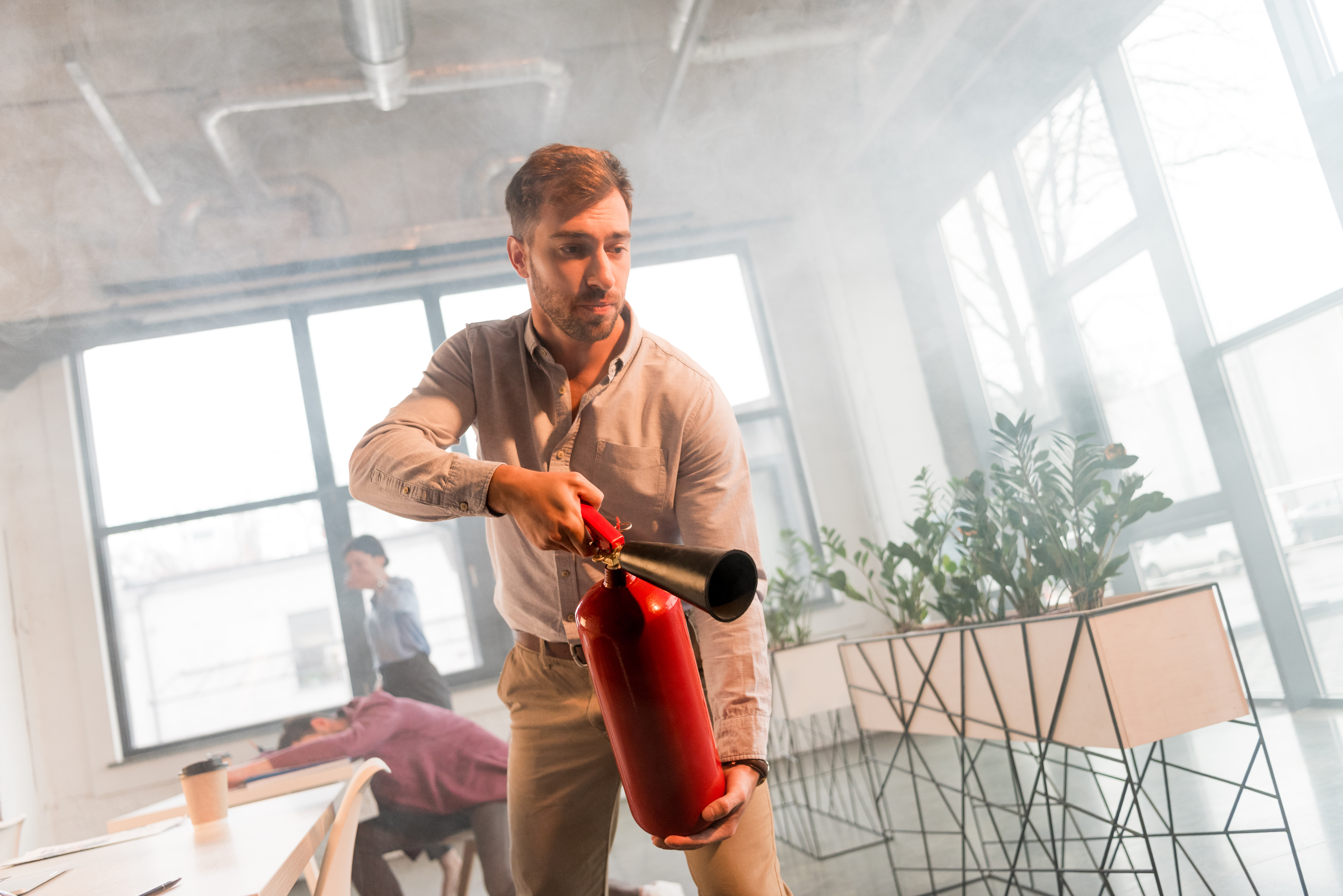 handsome businessman holding extinguisher in office with smoke near colleagues
